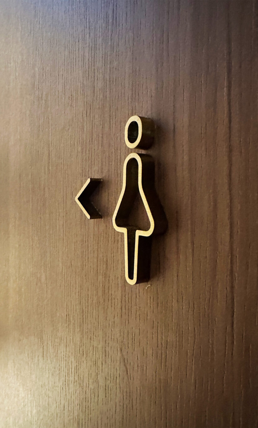 A signage of the toilet for women mounted on a wall showing restroom direction, a design innovation by Studio X