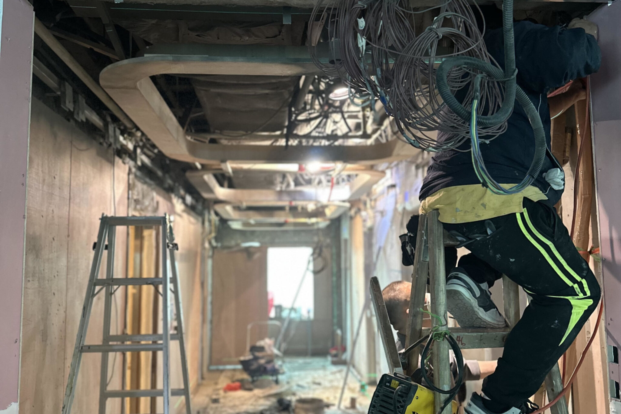 Maintenance engineer from Studio X working in a narrow pathway inside a building, fixing and rearranging wires and equipment