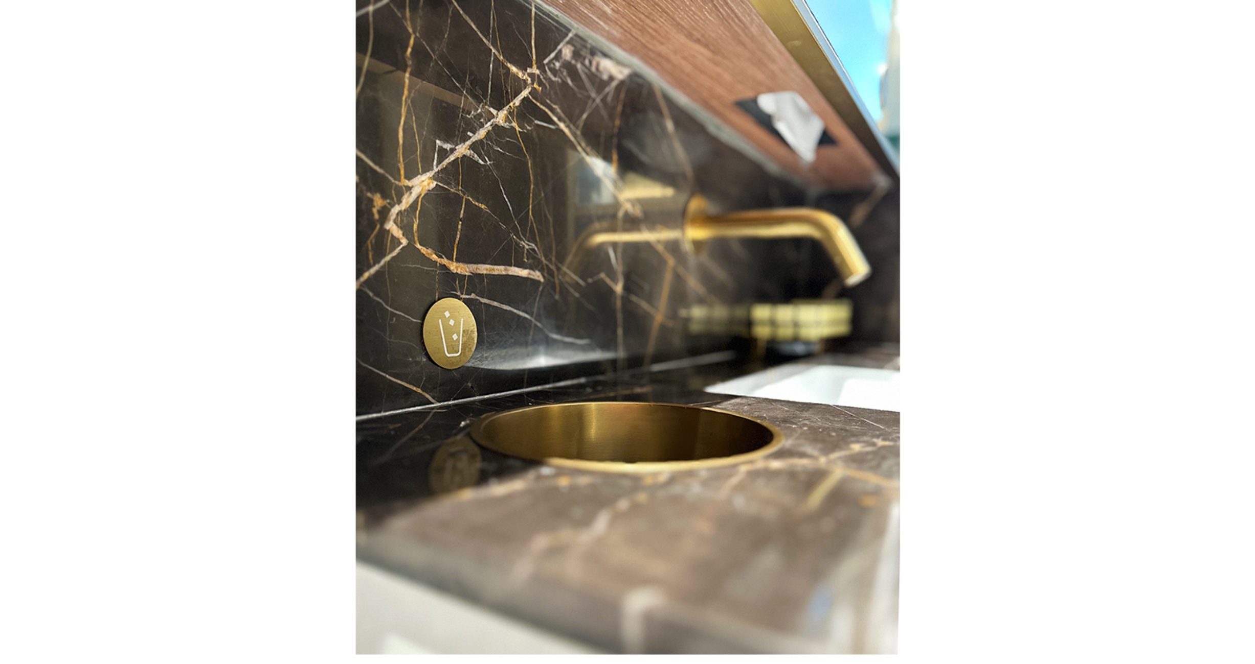 A close-up shot of a marble wash basin or water cooler with a wall-mounted button for glass filling, a project by Studio X